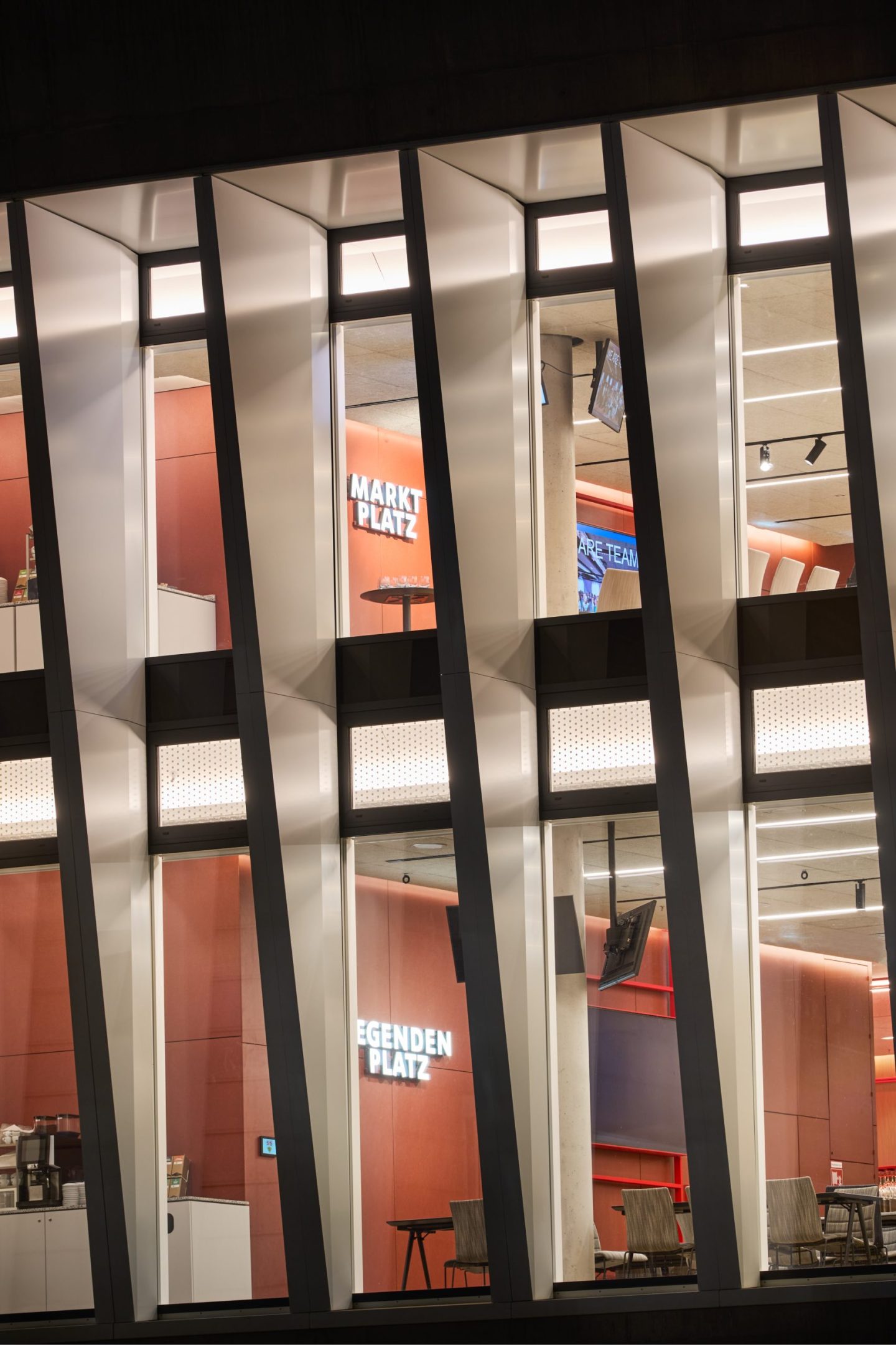 Exterior view of the VfB Stuttgart business lounge signage at MHP Arena, featuring illuminated destination graphics visible through the glazed stadium facade.