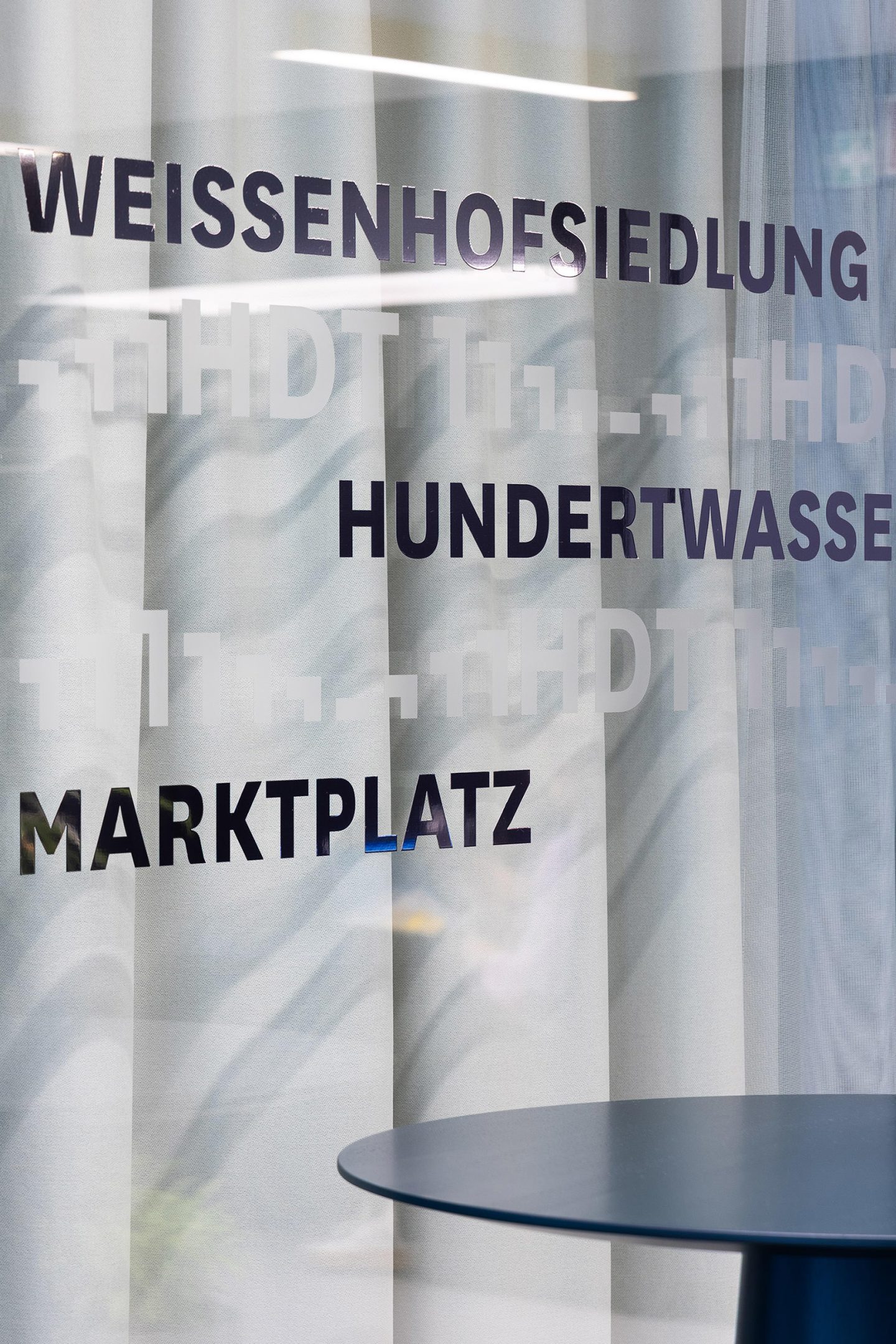 Signage for Haus des Tourismus Stuttgart, featuring typographic destination names applied to a translucent interior screen as part of the wayfinding system.