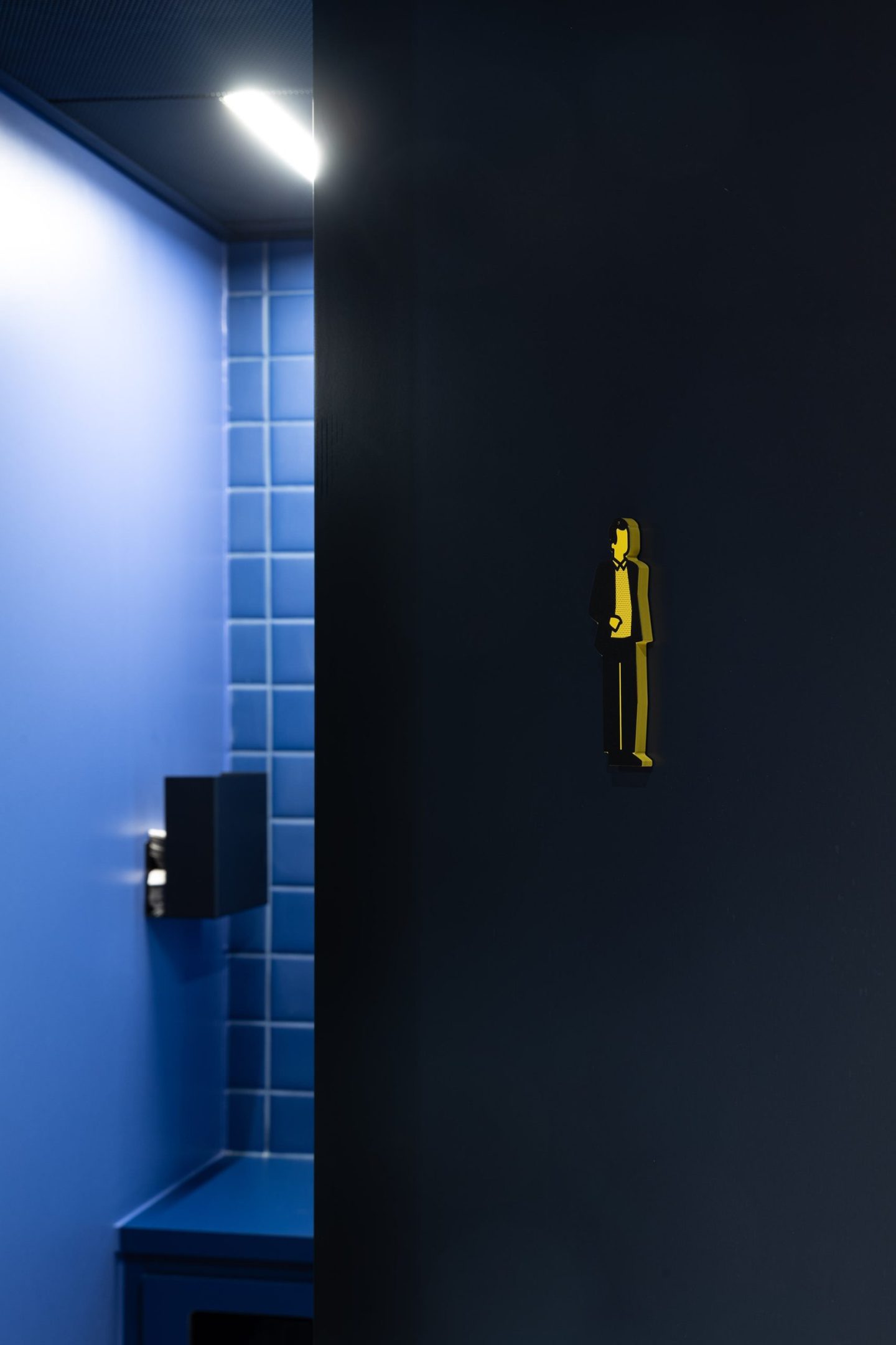 Restroom pictogram for Haus des Tourismus Stuttgart, featuring a custom yellow visitor icon applied to a dark blue door as part of the interior wayfinding system.
